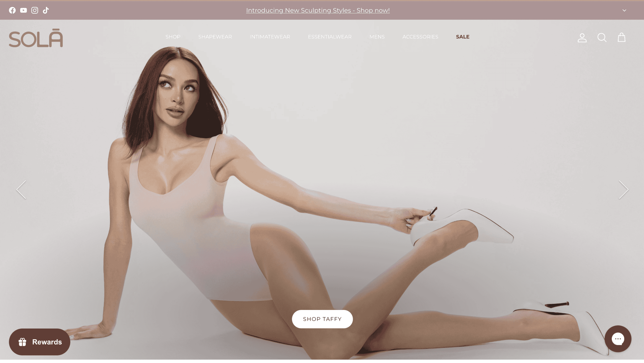 Russell Cariso posing in a white bodysuit with a high heel shoe.